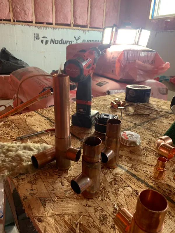 Several copper tees with short pipe sections soldered in, standing upright on the bench in front of an insulated basement wall.