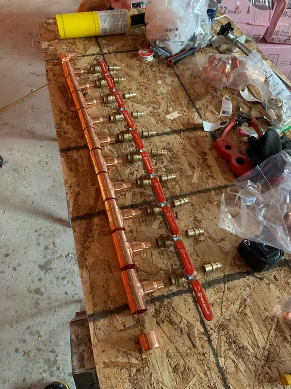 A long copper header with a row of outlets, red-handled ball valves and brass fittings laid out beside it on the workbench.